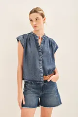 Camisa celeste de corte amplio, con mangas cortas y cuello redondo. Confeccionada en tencel, con cartera oculta en el delantero y botones metálicos con el logo de la marca.