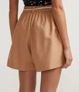 Short ancho color marrón claro, confeccionado en algodón, viscosa, modal y lino. Presenta pliegues y cordón trenzado en la cintura.