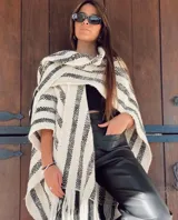 Ruana tejida a mano en telares, confeccionada en 100% lana Merino, con diseño a rayas horizontales en blanco y negro y flecos en el borde inferior.