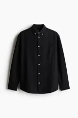 Camisa negra de algodón Oxford con cuello americano, tapeta clásica, bolsillo superior abierto y canesú en la espalda. Mangas largas con puños abotonados y bajo levemente redondeado. Corte estándar para una silueta clásica y cómoda.