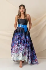 Vestido largo strapless con corpiño negro y falda estampada con degradé floral en tonos azules, violetas y blancos. Falda amplia con tablas y bolsillos, armada con tul y más larga atrás. Incluye cinturón azul con hebilla circular. Modelo único.