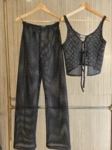 Conjunto de top y pantalón de hilo calado color negro. El top es corto con breteles finos y cierre frontal con lazos. El pantalón es de tiro alto y corte recto.
