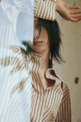 Camisa oversized de sarga color beige con rayas verticales marrones, cuello clásico, cierre frontal con botones ocultos, mangas largas con puños abotonados y bajo recto.