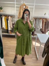 Vestido oversize color verde oliva, de pana fina, con cuello camisero, cierre frontal con botones, mangas cortas con puños arremangados y bolsillos laterales.