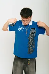 Chomba azul de piqué con cuello blanco, corte regular, manga corta con puños blancos, estampado con logo en la manga y bordado en el pecho.