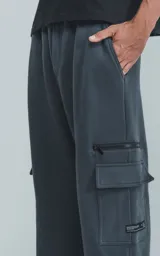 Pantalón de jogging gris oscuro, de corte amplio, con cintura y puños elásticos, bolsillos laterales y trasero, y bolsillo lateral adicional con cierre.