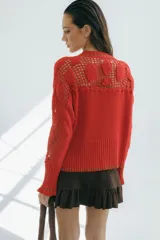 Cárdigan azul con detalles en crochet, mangas con volado y vivos de color rojo en cuello, puños y frente. Tiene botones al frente.