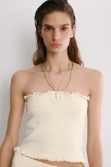 Top corto tipo bandeau de color blanco, con escote recto y hombros descubiertos. Presenta una textura elástica y acabados con bordes ondulados en el escote y el bajo.