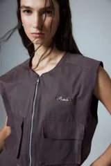 Chaleco corto color marrón confeccionado en gabardina con cierre metálico frontal, bolsillos con fuelle y badana de PU en la espalda.
