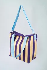 Bolso tipo tote bag con diseño a rayas verticales blancas y negras, doble asa de mano rosa y correa de hombro ajustable y removible también rosa.