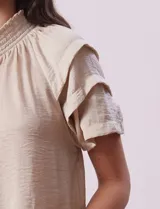 Blusa color beige de gasa estampada, marca Alex & Lili. Tiene cuello fruncido, escote en V con lazo y mangas cortas con volados.