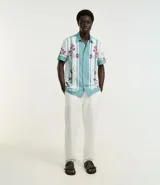 Pantalón de vestir blanco, de corte recto, con bolsillos laterales y traseros. Se ajusta a la cintura con cinturón de cuero marrón.