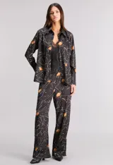 Pantalón pijamero de satén texturado color negro con estampado de flores amarillas y líneas blancas. Tiene calce relajado, cintura elastizada y bolsillos ocultos.