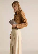 Chaqueta marrón de cuero gamuzado, con cuello camisero, cierre frontal con botones, dos bolsillos de parche delanteros y puños abotonados.