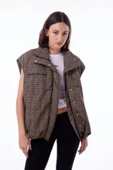 Chaleco puffer impermeable con estampado geométrico en tonos marrones y negros, forrado con tafeta negra. Tiene dos bolsillos frontales, bolsillos laterales ocultos, cierre desmontable, broches snap y elástico ajustable con tanca en ruedo.