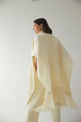 Ruana color crema de lana fina con flecos en el ruedo y bolsillos delanteros.