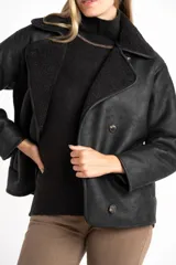 Chaqueta tipo gamulán de color negro con forro de corderito sintético al tono. Presenta solapas anchas, cierre frontal con botones y un diseño entallado al cuerpo.