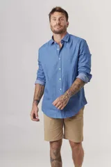 Camisa de manga larga azul denim, con cuello clásico y cierre frontal con botones. Mangas con puños abotonados y corte recto.