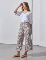 Pantalón capri de lino estampado con flores blancas sobre fondo marrón. Tiene pretina trasera elastizada y bolsillos delanteros.