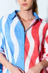 Túnica tipo vestido camisero corto con estampado de rayas onduladas verticales en colores rojo, blanco y azul. Tiene cuello camisero, cierre frontal con botones y mangas largas con puños abotonados.