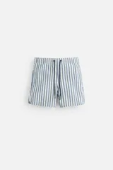 Bañador de hombre confeccionado en tejido técnico con textura, color blanco con rayas verticales azules y amarillas. Cintura elástica ajustable con cordón, bolsillos laterales y bolsillo trasero con solapa. Bajo con aberturas laterales y forro interior.