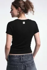 Remera negra de corte ajustado, mangas cortas y cuello redondo. Presenta frunces laterales que realzan la figura.