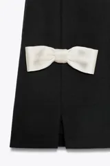 Vestido corto negro sin mangas, con cuello redondo y detalle de lazos blancos en la parte inferior.