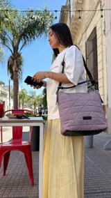 Cartera capitoneada color lila con diseño geométrico, asa de hombro negra y correa ajustable extraíble. Amplia y cómoda, ideal para el uso diario.