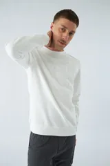 Buzo blanco de felpa con cuello redondo, mangas largas y puños. Presenta un estampado en relieve con texto y logo en goma.