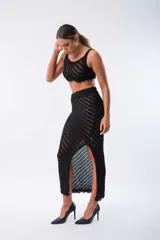 Conjunto de top y falda de tejido de punto calado color negro. El top es corto, de breteles anchos y terminación con flecos. La falda es larga, de tiro alto, corte recto y abertura lateral.