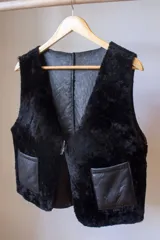 Chaleco marrón de cuero con interior de corderito color crema, cierre con gancho metálico y bolsillos frontales de corderito.