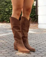 Botas texanas de caña media confeccionadas en cuero gamuzado color marrón. Presentan un diseño de corte clásico con costuras decorativas en el empeine, puntera levemente redondeada y taco bajo de madera.