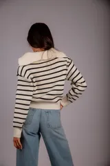 Sweater de punto color beige con rayas horizontales blancas, cuello polo con cierre de cremallera y mangas largas.