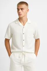 Camisa de lino color crudo, de manga corta, con cuello camisero y bolsillo de parche en el pecho.