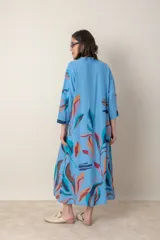 Vestido largo de lino color verde militar con estampado de hojas en tonos azul, naranja y marrón. Tiene cuello mao con botones, mangas tres cuartos y un bolsillo en el pecho.