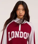 Suéter corto de punto con cuello alto y medio cierre con cremallera. Tiene mangas largas con sisa raglán y lettering "London" en el frente.