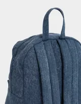Mochila azul de denim con bolsillo frontal con cierre y tirador con charms decorativos. Tiene correas regulables, manija superior y cierre superior.