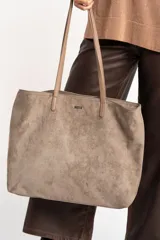 Bolso tipo tote de gamuza vegana color camel, con asas de mano y logo grabado en el frente.