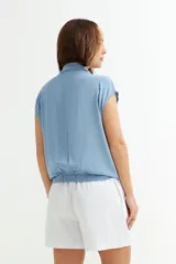 Camisa celeste con cuello, abotonada al frente y mangas cortas.