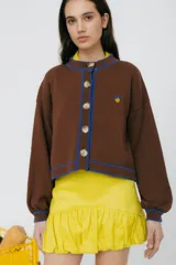 Cárdigan tejido en 50% algodón y 50% acrílico, color crema, con pespuntes tejidos en contraste color borgoña y bordado de limón en el pecho. Tiene cuello con volados, cierre frontal con botones y corte relajado.