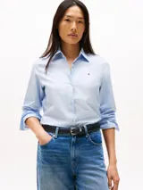 Camisa celeste a rayas verticales finas, confeccionada en popelina de algodón elástico. Tiene cuello inglés a contraste, puños a contraste, bajo camisero y logo de Tommy Hilfiger bordado en el pecho.