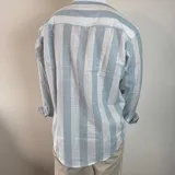 Camisa celeste y blanca a rayas verticales, de lino, con cuello mao y mangas largas con puños.
