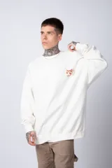 Buzo color crema de corte oversize confeccionado en tela friza con cuello redondo y puños y cintura acanalados. Presenta un pequeño bordado en el frente y un estampado grande en la espalda.