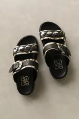 Sandalias bajas de cuero marrón con doble tira, hebilla ajustable y apliques de tachas metálicas.