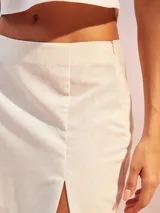 Falda corta color crema o blanco roto, de tiro alto, con abertura lateral en el ruedo.