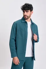 Camisa de manga larga color verde azulado, con cuello camisero, botones frontales y dos bolsillos de parche con tapa en el pecho.