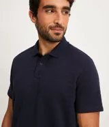 Polo azul marino de corte regular, confeccionada en algodón con textura de rayas horizontales. Tiene cuello inglés, botones en el pecho y mangas cortas.