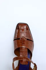 Sandalias de cuero color borgoña con textura croco, diseño cerrado en la parte delantera con aberturas laterales, punta cuadrada y cierre con hebilla ajustable en el tobillo. Taco ancho de 3 cm.