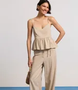 Blusa sin mangas color beige, con escote en V, breteles finos ajustables y peplum con volados en el bajo. Presenta lastex fruncido en la espalda.