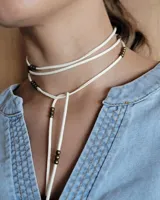 Collar marrón de cuero con cuentas doradas, con tiras finas que se atan al cuello y caen sobre el pecho.
